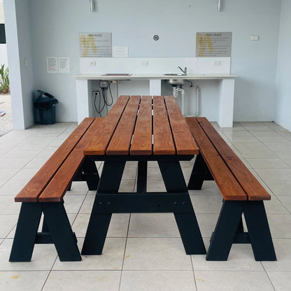 A wooden picnic table with attached benches, featuring medium brown wood slats and black wooden A-frame legs, set in a tiled outdoor patio area.
