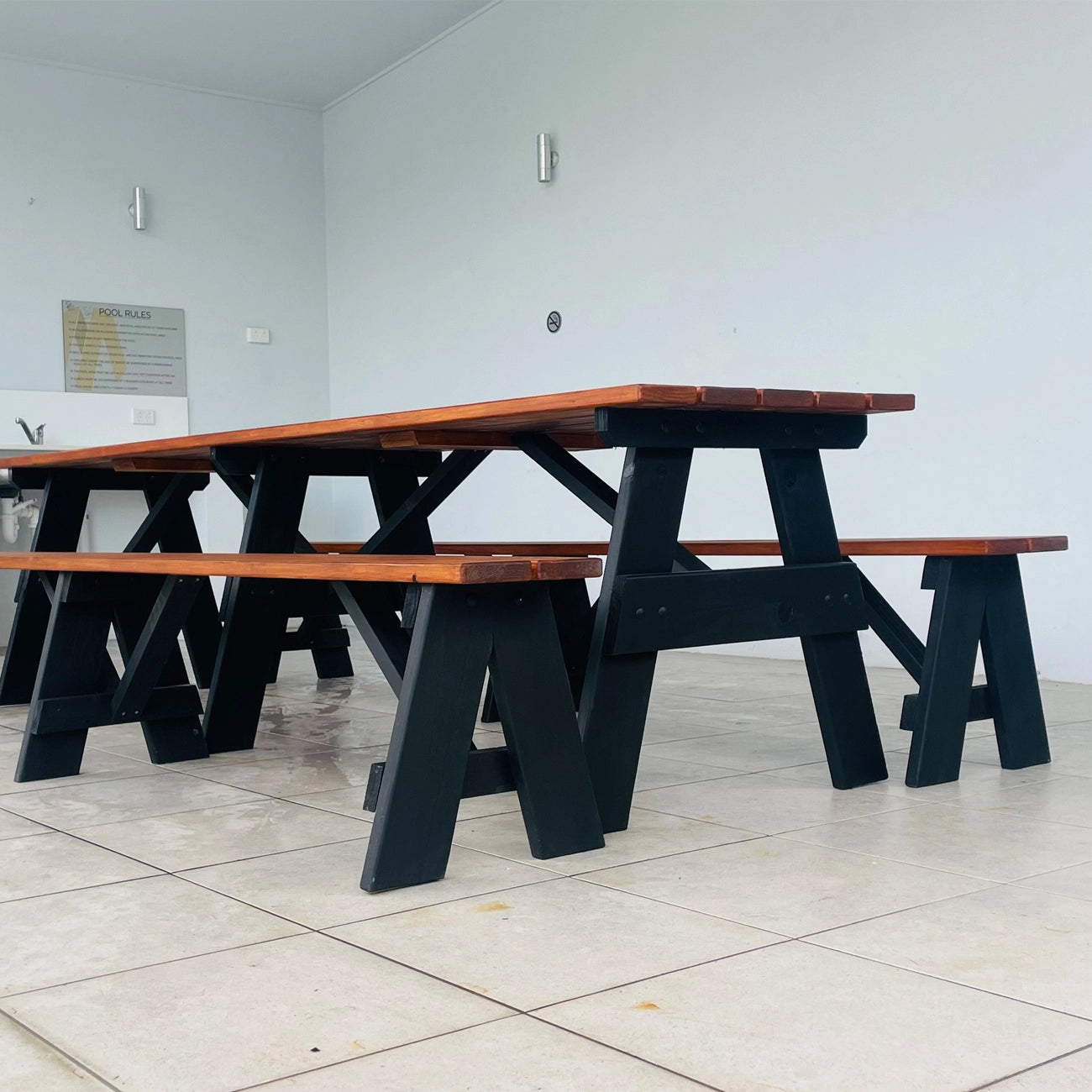 A black and brown wooden picnic table with matching benches, set in a minimalist room with light gray walls and tiled floor.