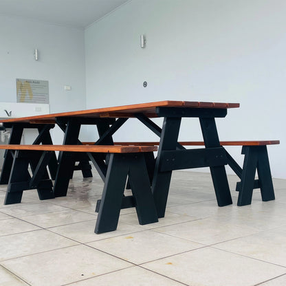 A black and brown wooden picnic table with matching benches, set in a minimalist room with light gray walls and tiled floor.