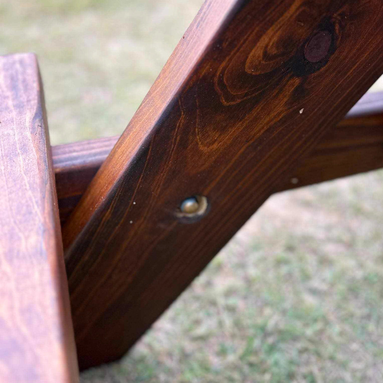 Close-up of a dark stained wooden chair frame with visible wood grain and a metal fastener, photographed outdoors on grass. Children sized picnic table handmade by JJ TImber Design