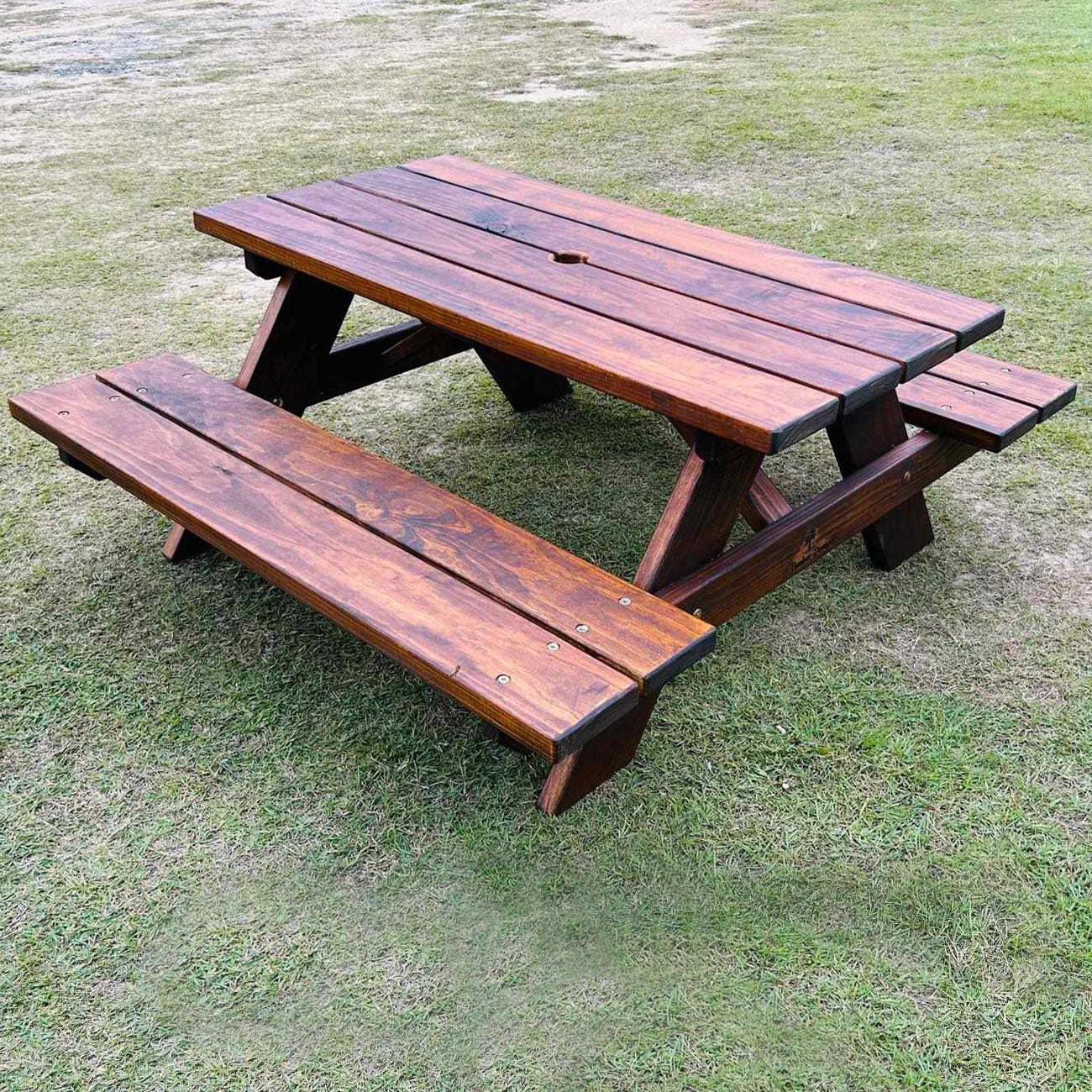 A dark brown wooden child sized picnic table with attached benches, placed on a grassy lawn. Handmade Picnic bench by JJ Timber Designs