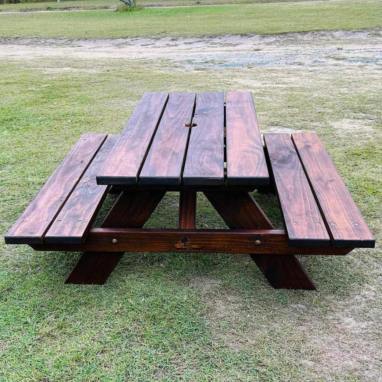 A dark brown wooden Children picnic table with attached benches, set outdoors on a grassy lawn. Handmade by JJ Timber Designs