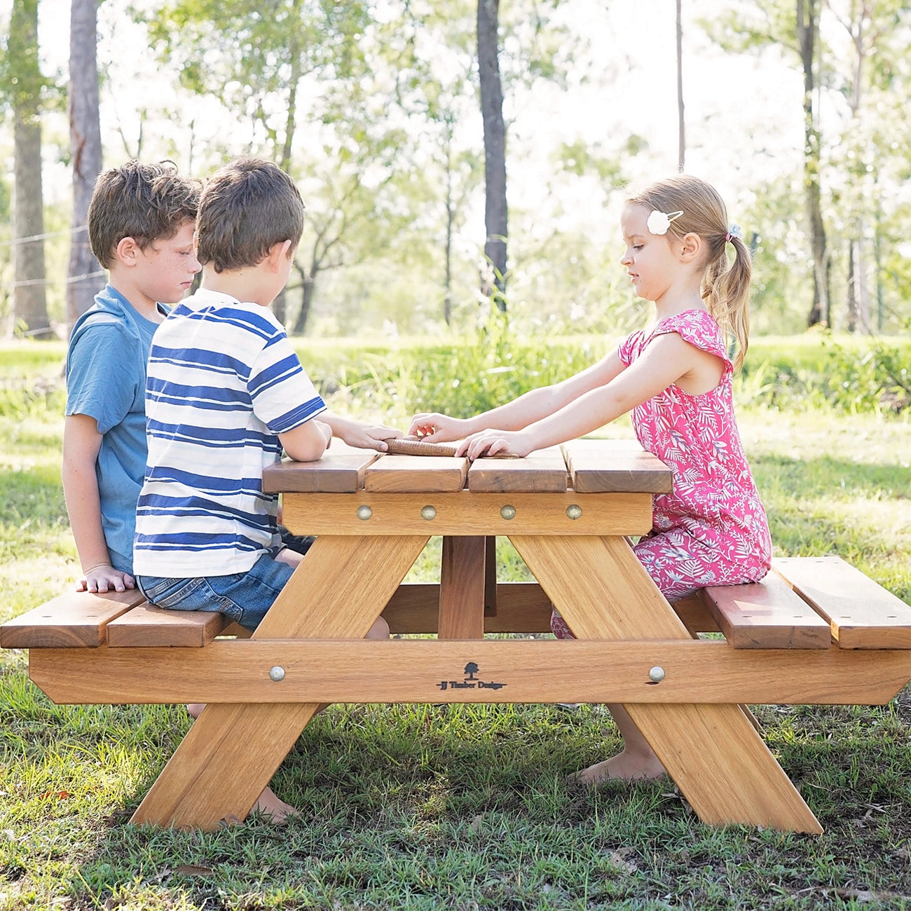 Children seated at JJ Timber kids picnic table in outdoor playground setting.