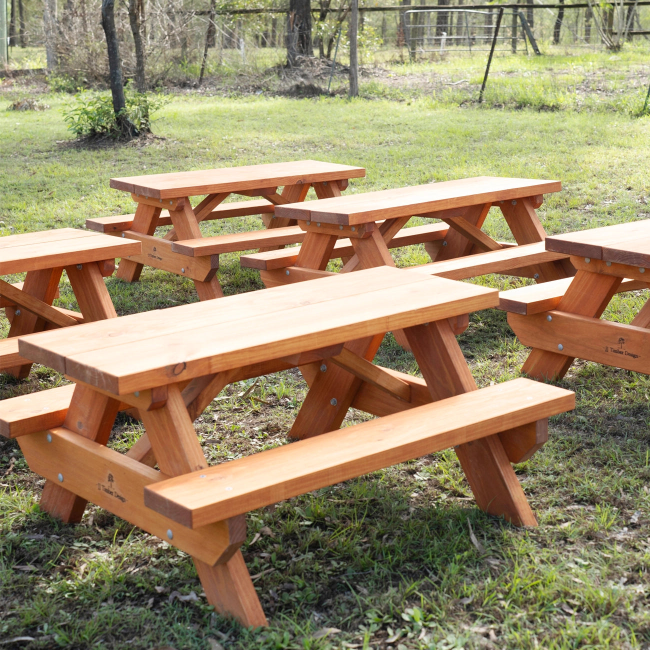 Several JJ Timber kids picnic tables arranged outdoors on grass.