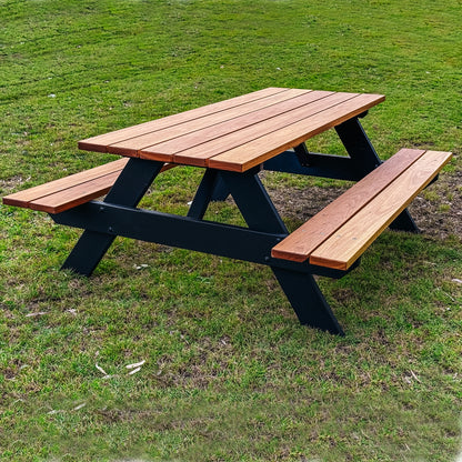 A picnic table with attached benches made of reddish-brown wooden slats and a black wooden frame, set on a green grass lawn. Handmade by JJ Timber Design