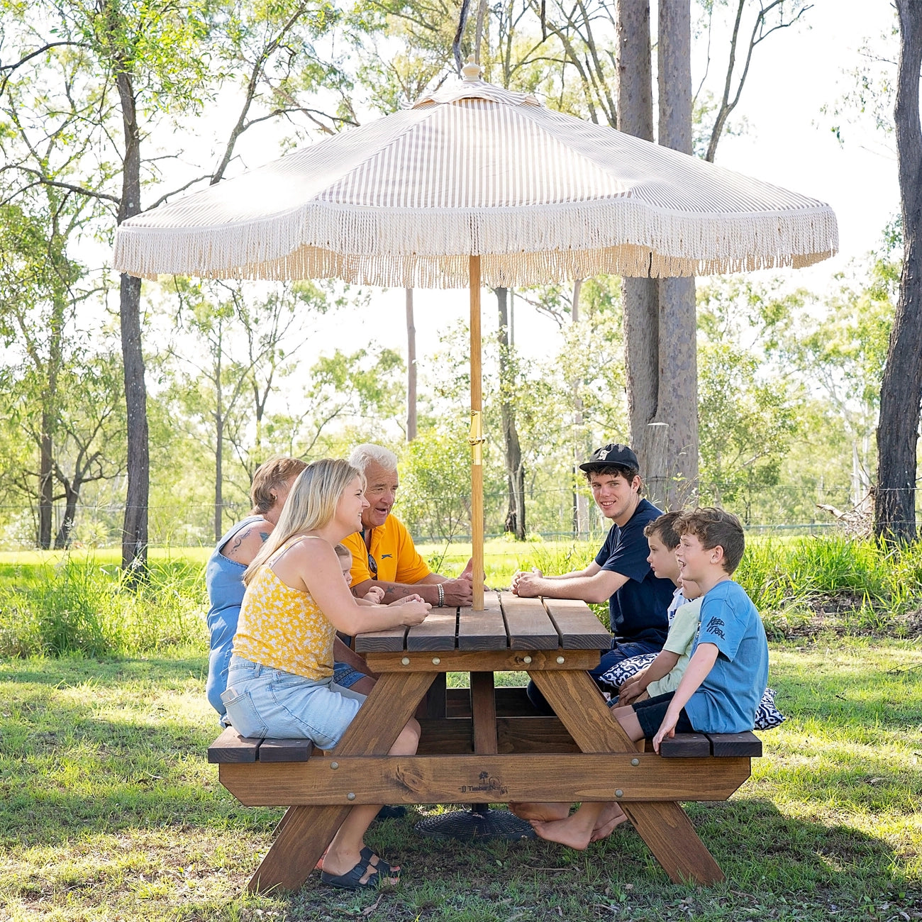 Family gathering around JJ Timber 2.4m heavy duty picnic table in natural park setting.