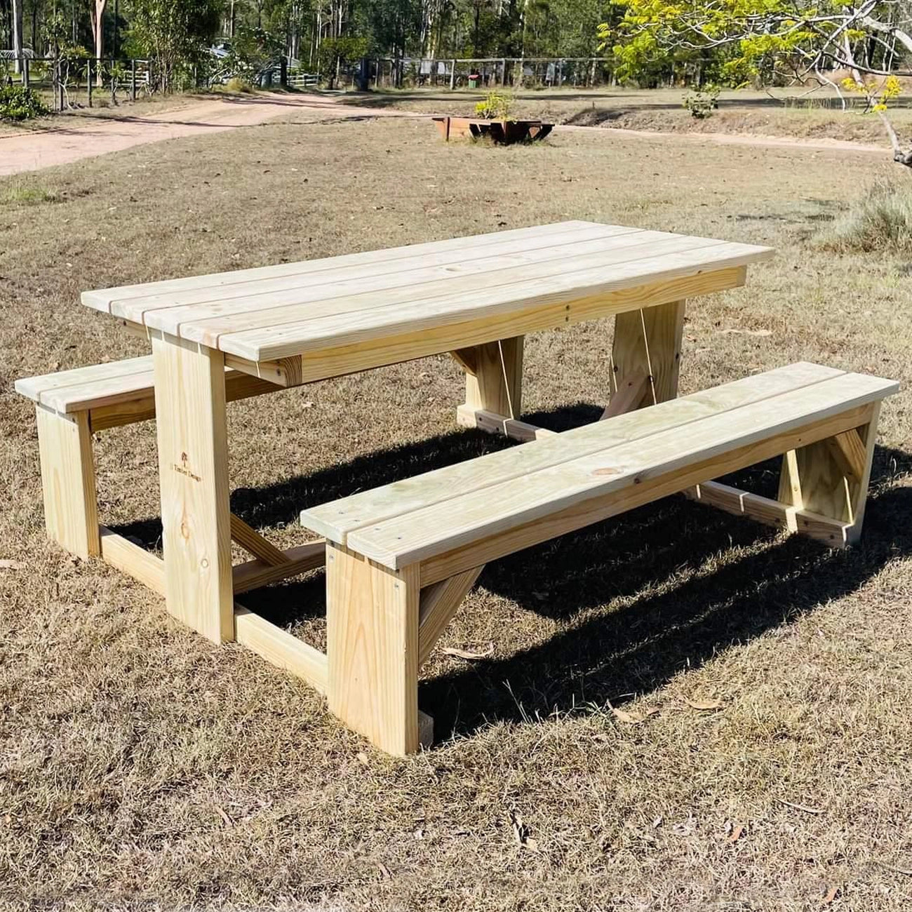 Light-coloured JJ Timber Design picnic table positioned on an asphalt driveway.