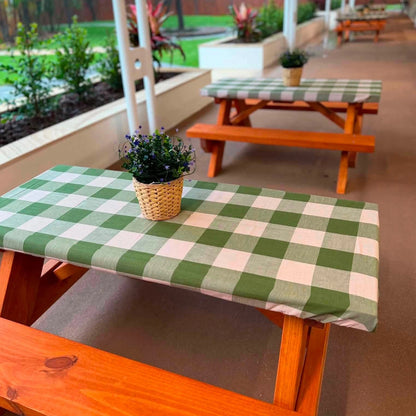 A green and white checkered tablecloth on a wooden picnic table, with a small potted plant in a woven basket on top, set in an outdoor patio environment. JJ Timber Design Picnic Tables