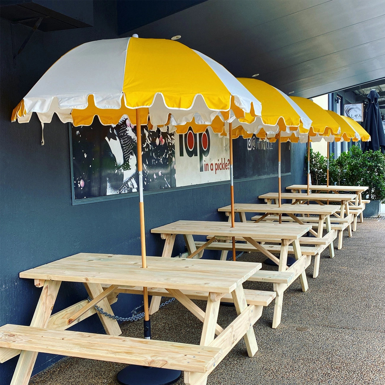 JJ Timber Design timber picnic tables under branded umbrellas at a food venue.