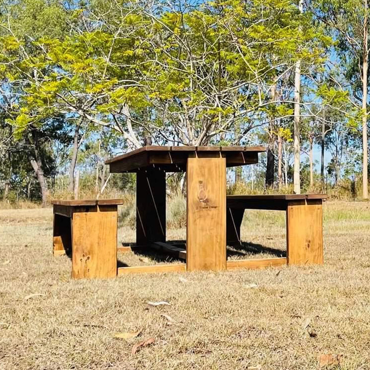 A rustic wooden picnic table with a matching bench in an outdoor grassy field with trees in the background.