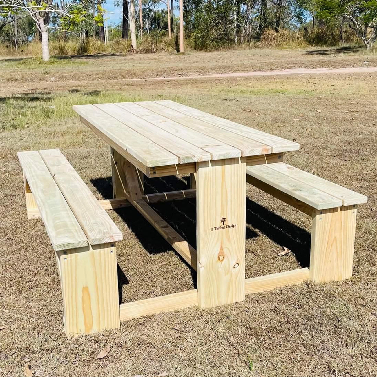 Two light timber JJ Timber Design picnic tables placed in an open outdoor field.