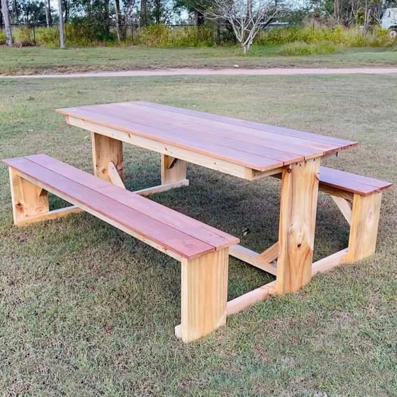 Natural treated pine and red-toned merbau JJ Timber Design picnic table with matching long benches on a grassy field.