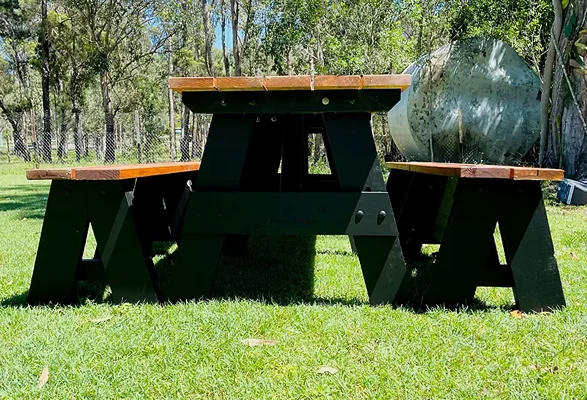 Dark timber JJ Timber Design picnic table with black supports in a sunny park.