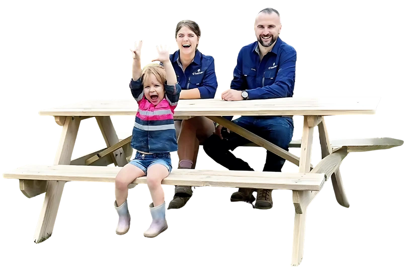 Family seated on a JJ Timber Design picnic table in an outdoor field.