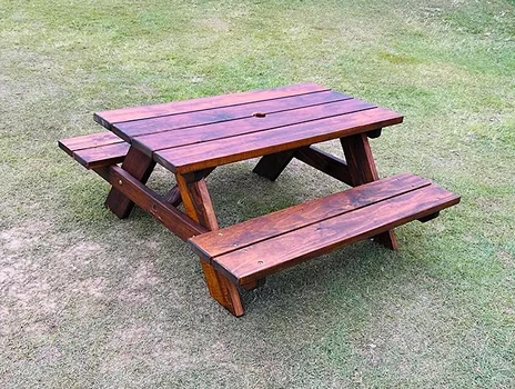 Stained JJ Timber Design picnic table glowing in full sunlight on grass.