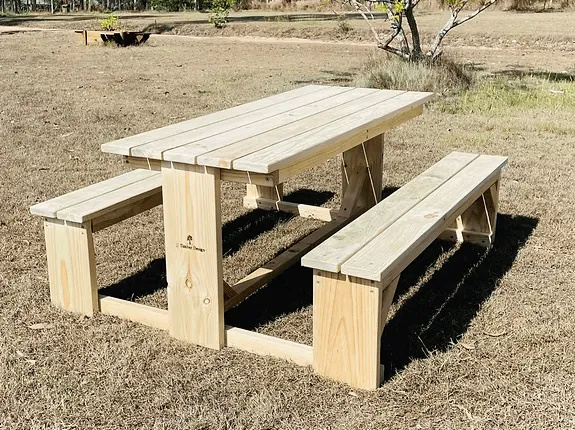 Light-coloured JJ Timber Design picnic table positioned on an asphalt driveway.
