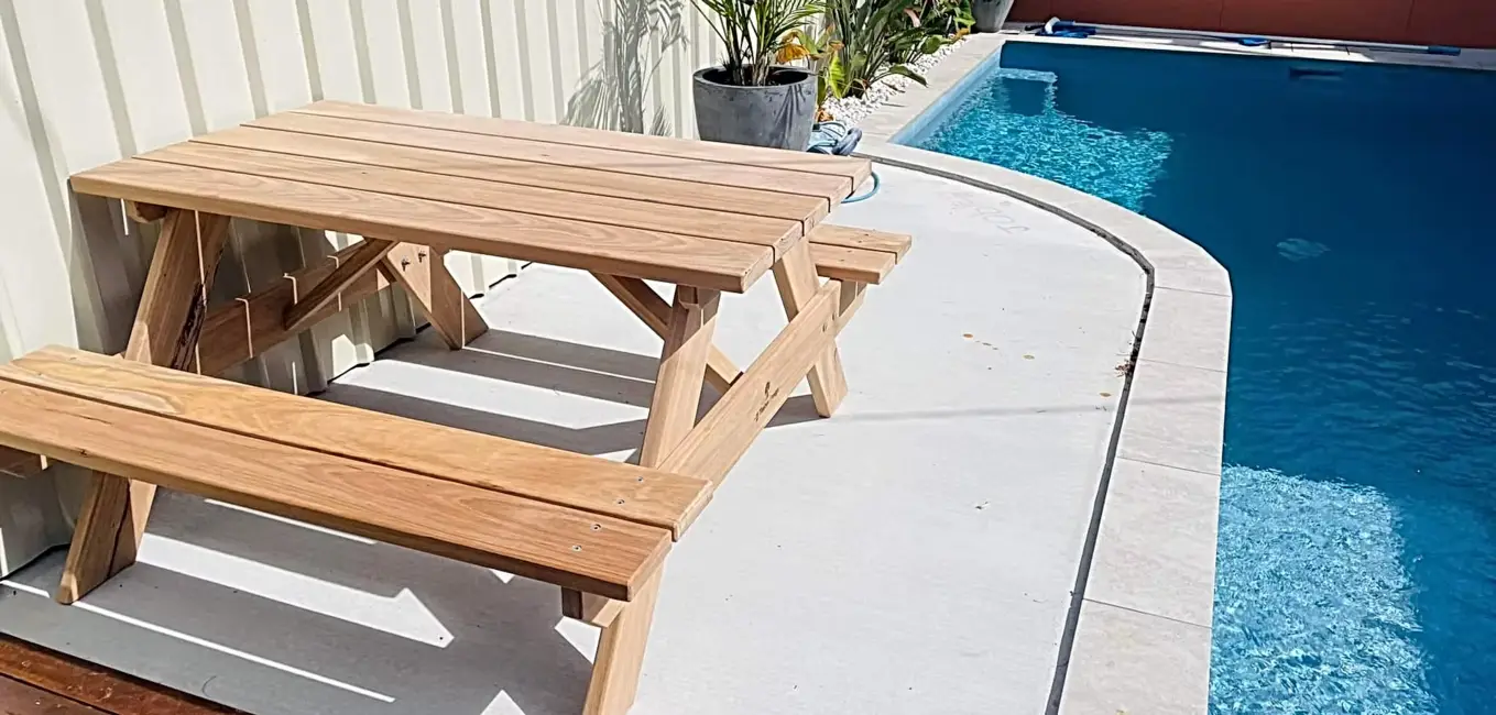 Natural JJ Timber Design picnic table on concrete patio near a pool.