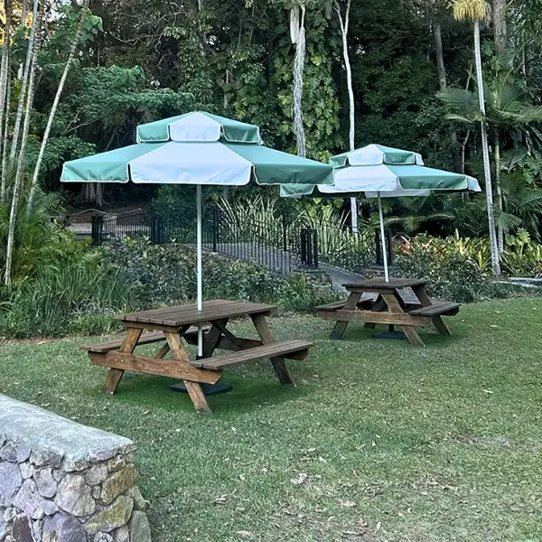 Outdoor dining area with JJ Timber Design picnic tables under green umbrellas.